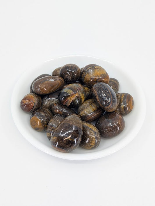Yellow Tiger Eye tumbled stones in white dish showing chatoyant golden shimmer