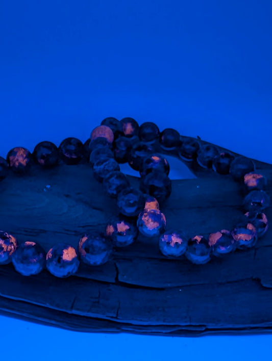 Two Yooperlite bracelets glowing bright orange under UV light on wooden driftwood background