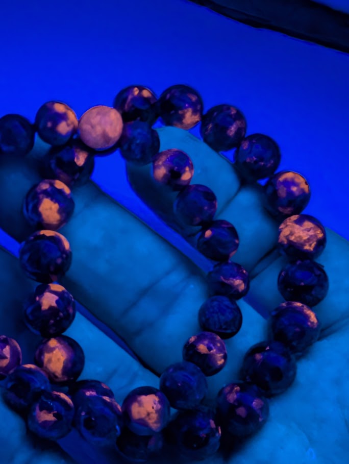 Close-up of Yooperlite bracelet held in hand, showing vivid orange fluorescence under UV light