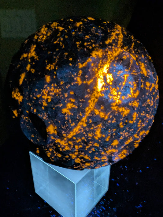 A massive 210 mm (8.27 in) Yooperlite carved moon sphere glowing intensely orange under UV light, highlighting natural sodalite inclusions.