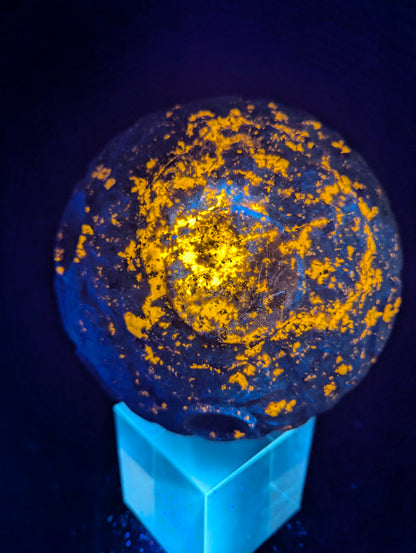 Extra-large Yooperlite carved moon sphere displaying vibrant orange fluorescence across deep hand-carved lunar craters under UV illumination.