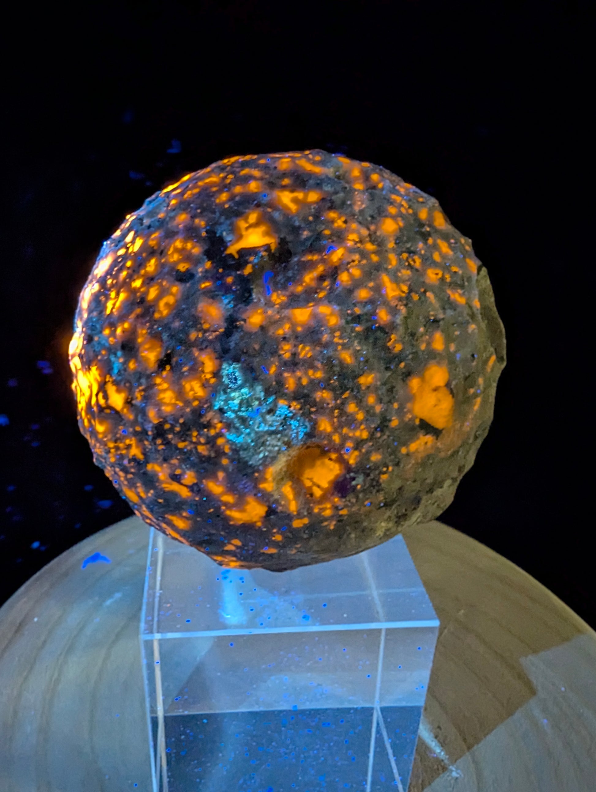 intense orange fluorescence of sodalite inclusions on a 98 mm (3.86 in) carved Yooperlite moon sphere under UV illumination.