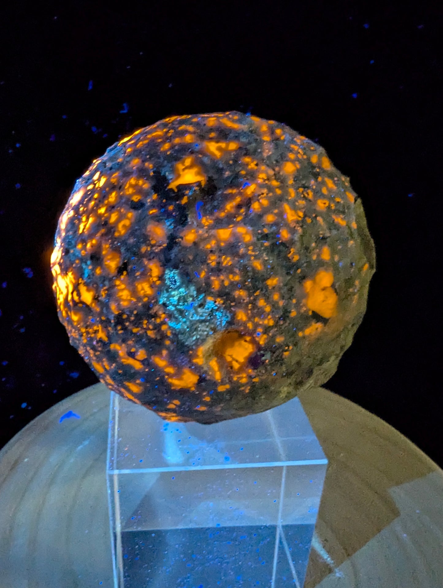 ntense orange fluorescence of sodalite inclusions on a 98 mm (3.86 in) carved Yooperlite moon sphere under UV illumination.