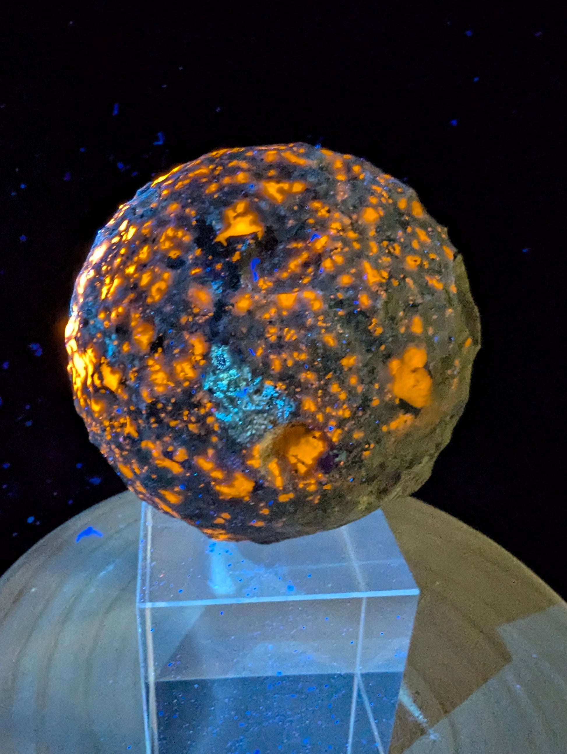 ntense orange fluorescence of sodalite inclusions on a 98 mm (3.86 in) carved Yooperlite moon sphere under UV illumination.