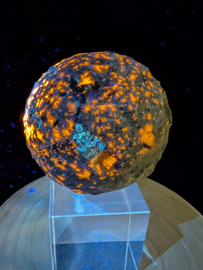 ntense orange fluorescence of sodalite inclusions on a 98 mm (3.86 in) carved Yooperlite moon sphere under UV illumination.