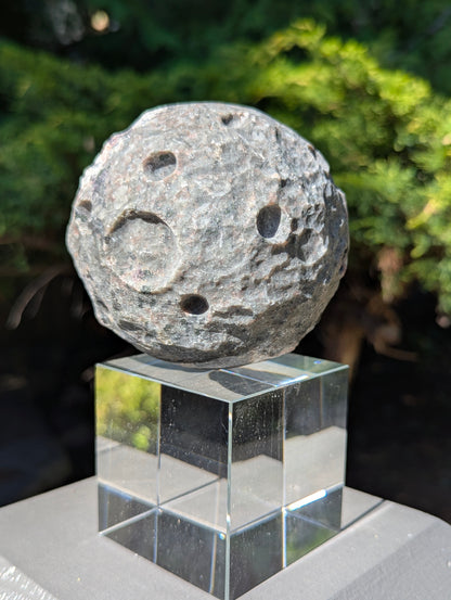 A 98 mm (3.86 in) Yooperlite carved moon sphere in natural sunlight, showing its grey syenite matrix and hand-carved craters.