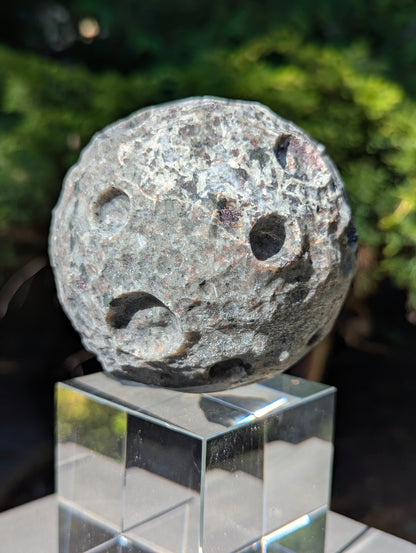 A 98 mm (3.86 in) Yooperlite carved moon sphere glowing bright orange under UV light on an acrylic display stand.