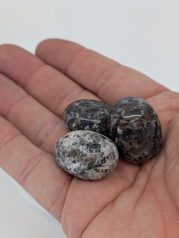 Hand holding Yooperlite tumbled stones showing surface detail and natural color