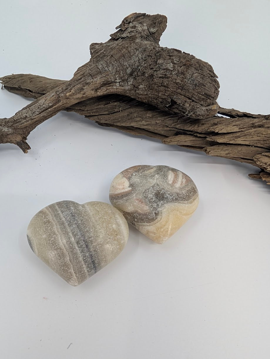 Pair of Zebra Calcite hearts showing cream and grey banding on driftwood.