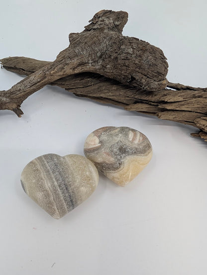 Pair of Zebra Calcite hearts showing cream and grey banding on driftwood.